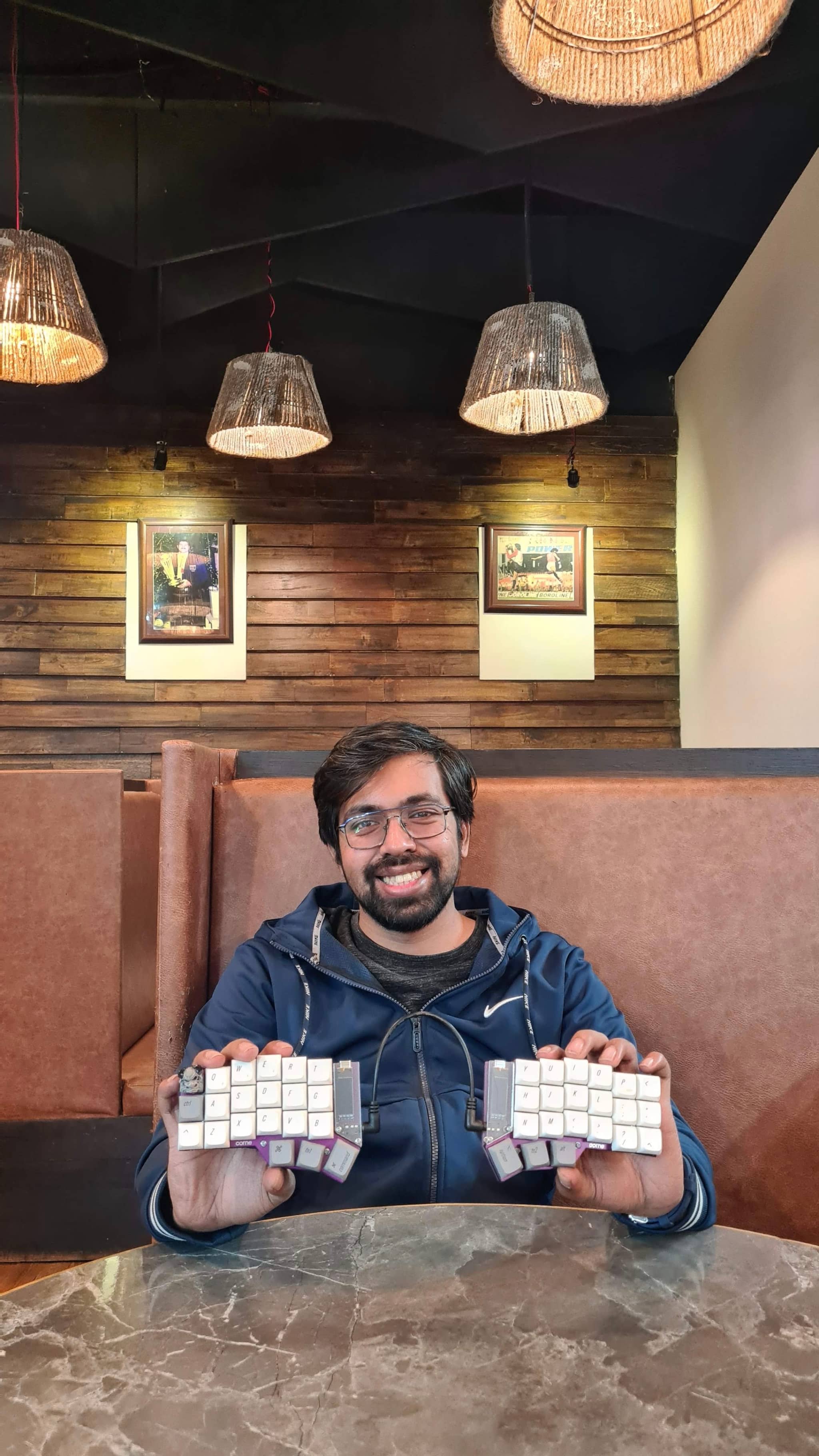 The image is split into two halves. On the left side, we see a person sitting at what appears to be a dining table, holding up several rectangular objects that resemble candles or possibly small blocks with inscriptions. This person has short dark hair and is wearing a blue shirt.

On the right side of the image, there's an interior view of a room with a dark ambiance, possibly a restaurant or bar due to the presence of a bar counter with stools and a wall-mounted light fixture. The focus of the right image is on these objects, which are not clearly distinguishable due to the distance and angle.
