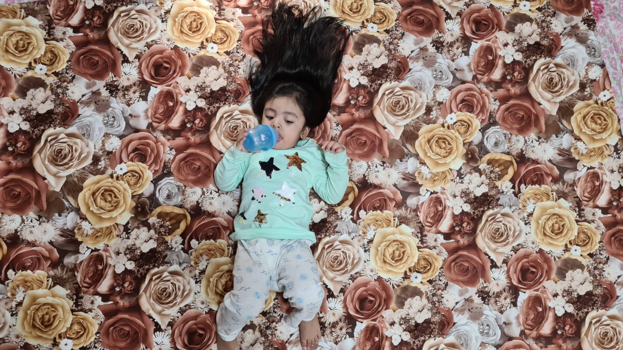 A colorful patterned with numerous roses, with a child laying in it, captured by an overhead angle.