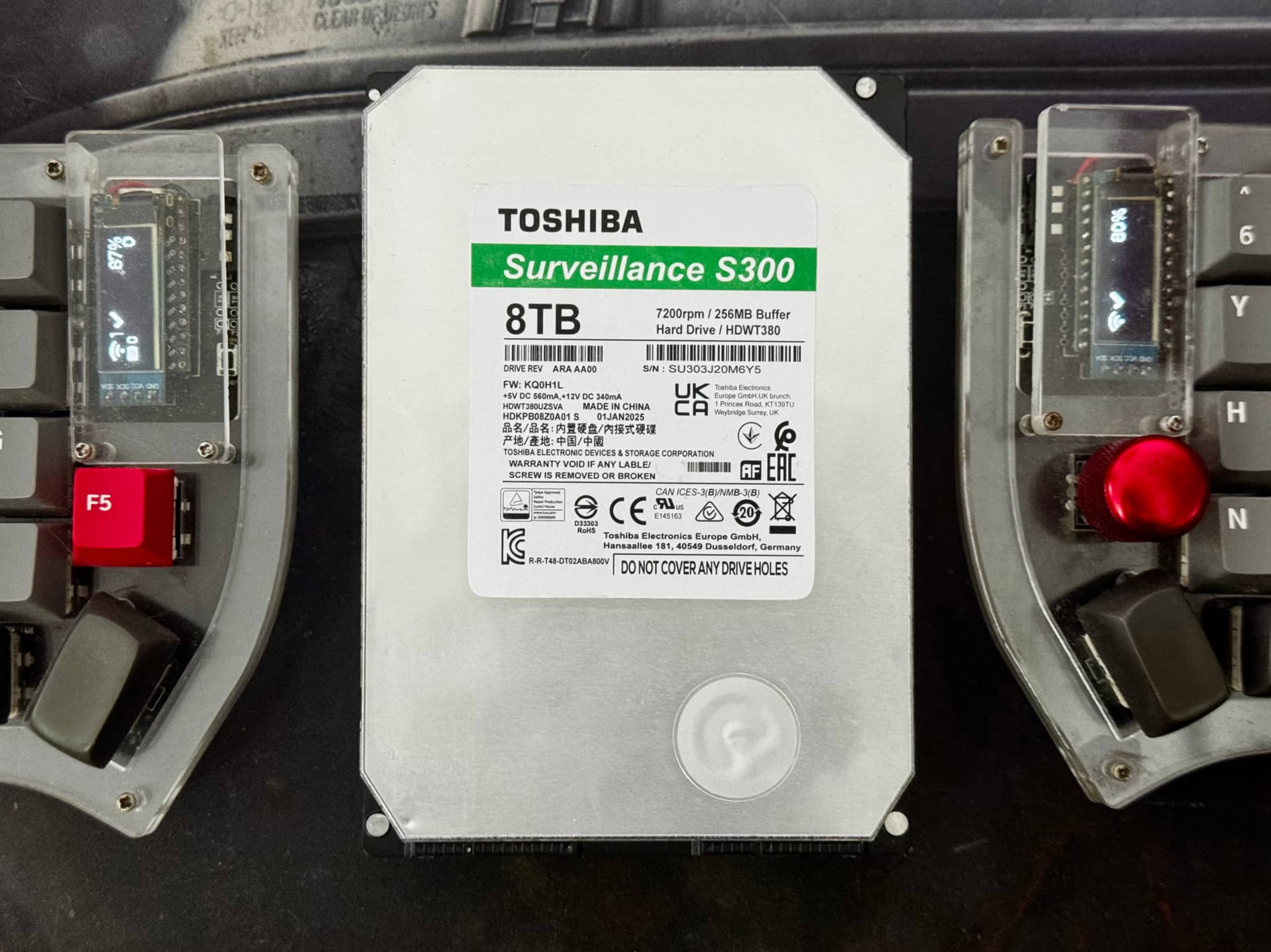 The image shows an electronic device with an attached battery pack and some control panels, possibly for a vehicle. The device has various buttons and switches, and there are visible brand names like Toshiba and others that are not fully visible.