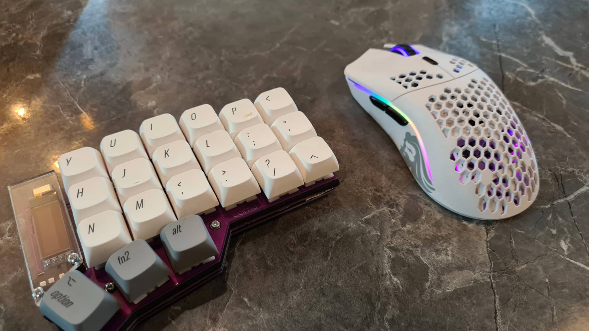 The image displays a computer keyboard and mouse with additional mechanical keycaps, designed to resemble the shape and layout of the actual keys. These new keycaps have a different color scheme and are arranged in rows, suggesting they might be custom-designed for specific tasks or preferences. The mouse appears to have integrated buttons or functions on its side, also in a contrasting color. Both items are placed on a table or countertop with a blurred background.