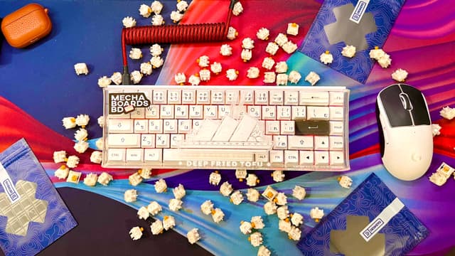 The image displays a computer keyboard with some keys removed, placed on top of what appears to be a small heap of candy. There's also a computer mouse nearby. In front of the keyboard, there are confetti pieces scattered about, creating a festive atmosphere. To the left side of the keyboard, there is a small bottle that could contain alcohol or some other liquid, but it's not entirely clear from this angle. The overall setting seems to be a casual workspace with a bit of celebration or celebration-inspired decorations.