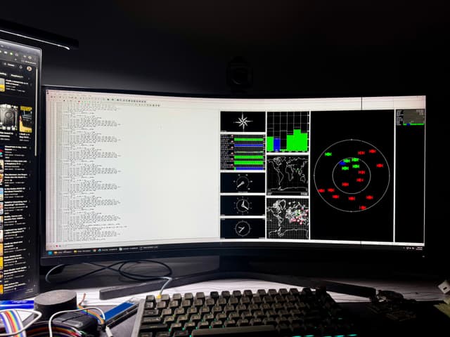 The image features a computer desktop with a variety of open applications and windows. On one side, there's a screenshot of what appears to be a complex software interface, possibly related to scientific data visualization or control systems, with numerous graphs and charts displaying various data points. The other side of the screen shows a more typical user environment, featuring web browser tabs open in Microsoft Edge, indicating that the user is multitasking between work and personal browsing. Additionally, there are two monitors visible; one at the top with a different interface and another below it, likely displaying additional data or applications. The user's peripherals include a keyboard partially visible on the right, and the mouse is also just out of frame on the left side of the image.