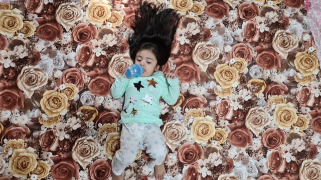 A colorful patterned with numerous roses, with a child laying in it, captured by an overhead angle.