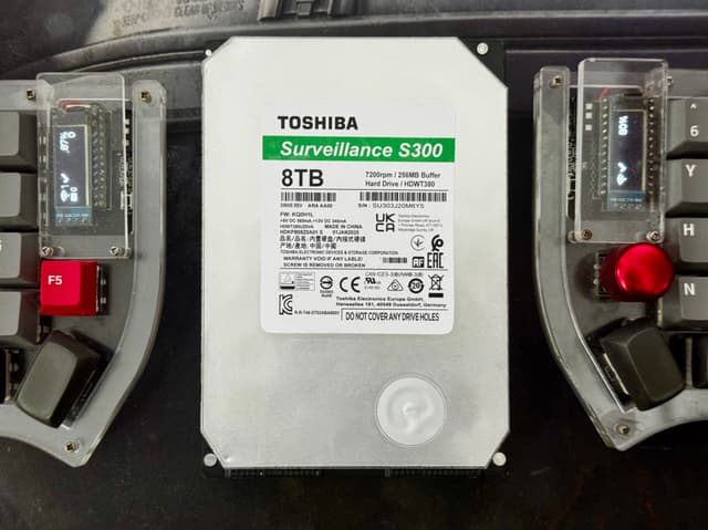 The image shows an electronic device with an attached battery pack and some control panels, possibly for a vehicle. The device has various buttons and switches, and there are visible brand names like Toshiba and others that are not fully visible.