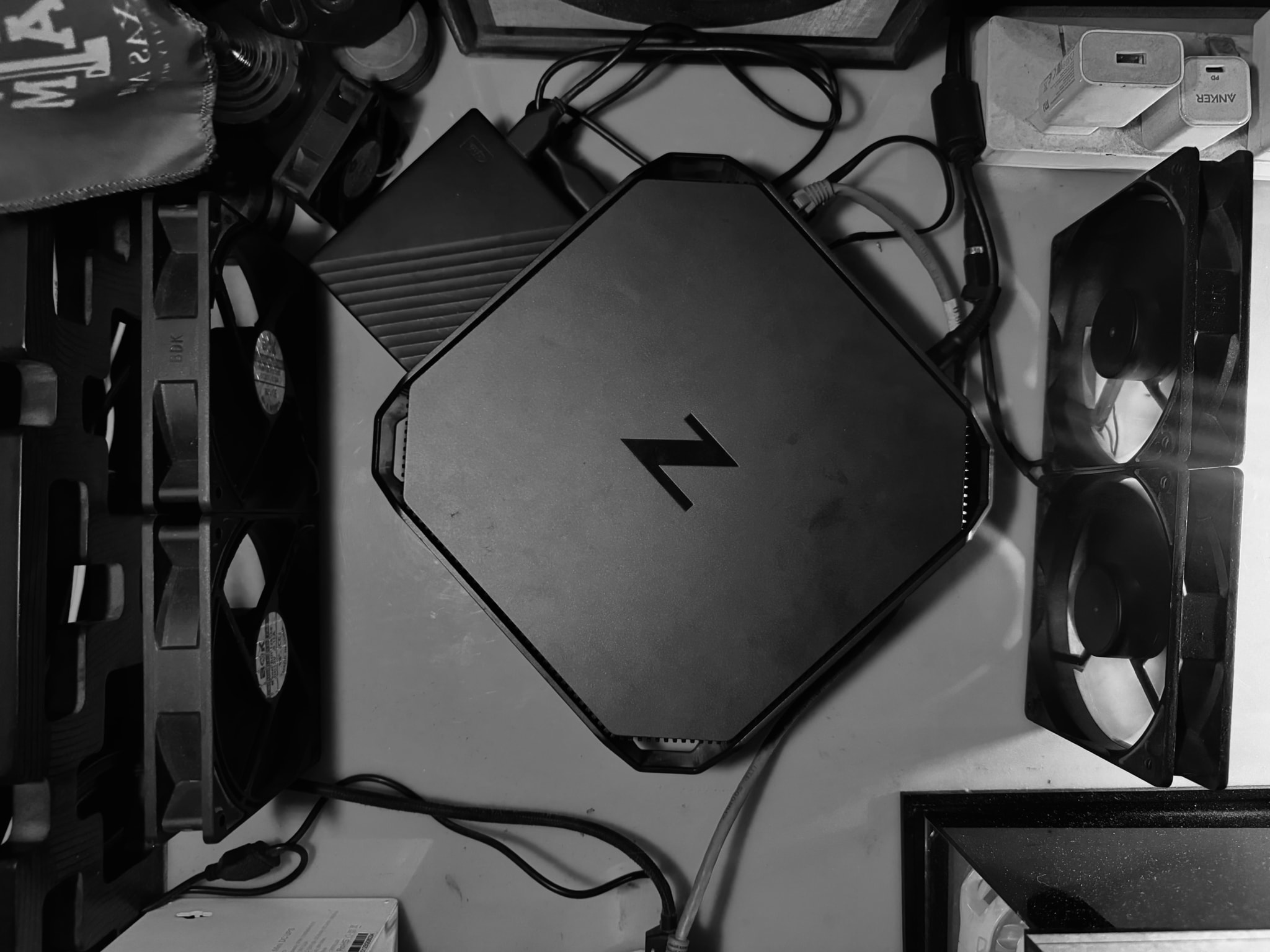 The image features a computer setup on a table. It includes several components, such as a central processing unit (CPU), a video card (GPU), and a storage device. There are also cables and what appear to be peripherals like a keyboard or a mouse. The setup is somewhat disorganized, with various items scattered around.